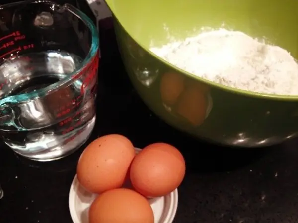 Eine grüne Schüssel mit Mehl und Wasser sowie drei Eier in einer kleinen Schale, bereit zum Kochen von Nudel-Hackfleischrolle.