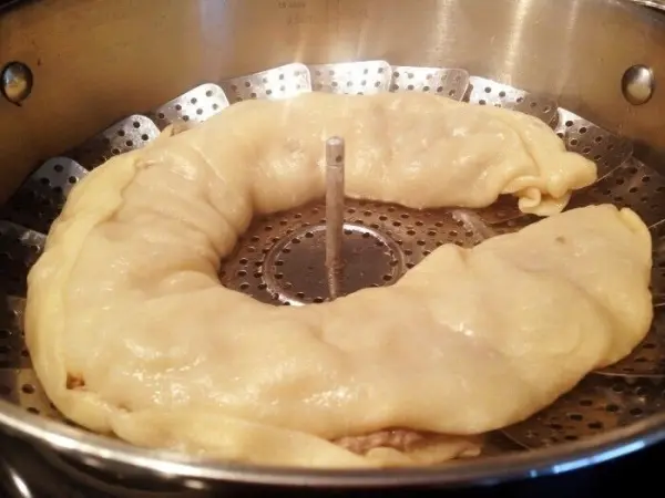 Eine Nudel-Hackfleischrolle wird gedämpft und liegt spiralförmig in einem Dämpfer, umgeben von dampfendem Wasser.