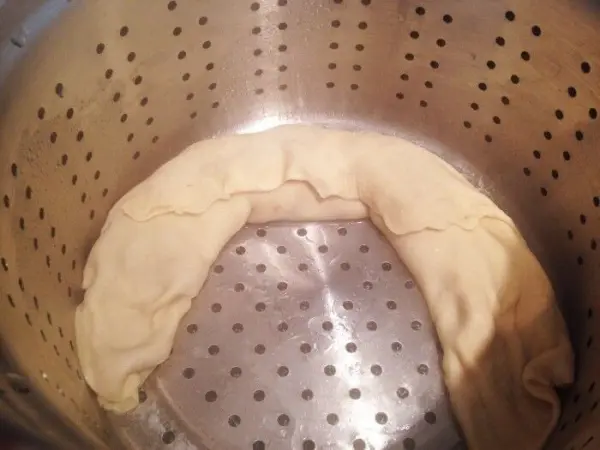 Eine ruhige Nudel-Hackfleischrolle liegt in einem Dampfgareinsatz und wartet darauf, gegart zu werden.