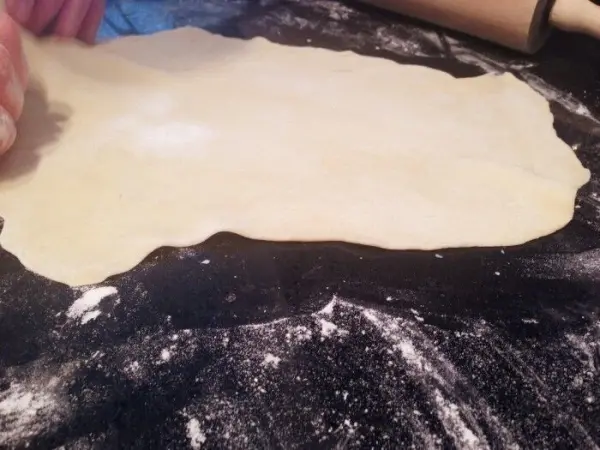 Ein ausgerollter Teig liegt auf einer bemehlten Arbeitsfläche, während eine Hand ihn sorgfältig bearbeitet.