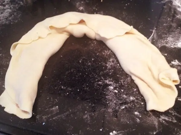 Eine geformte Nudelrolle mit Hackfleisch liegt auf einer bemehlten Arbeitsfläche, bereit zum Weiterverarbeiten.