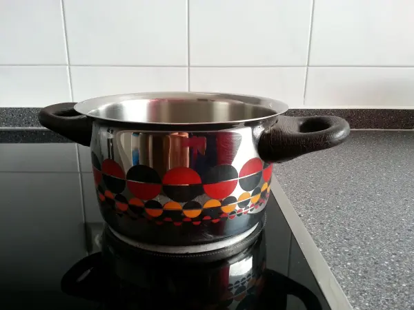 Ein bunter Kochtopf steht auf einem Herd und könnte durch Dampfen statt Bügeln Stoffe glätten, während die Umgebung minimalistisch wirkt.