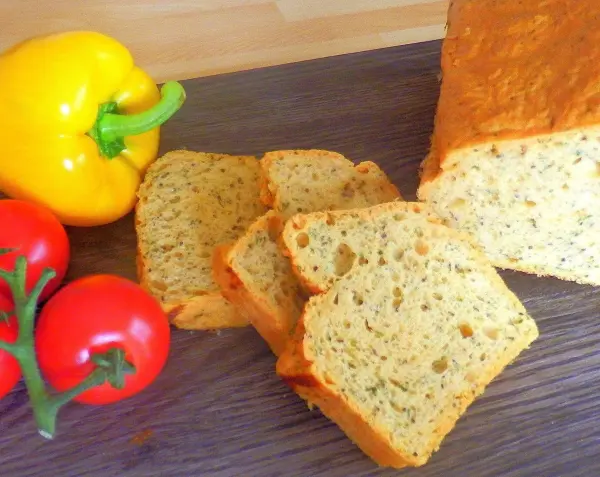 Das gesunde Brot aus rotem Linsenmehl steht auf einem Holzbrett, umgeben von frischen Tomaten und einer gelben Paprika.