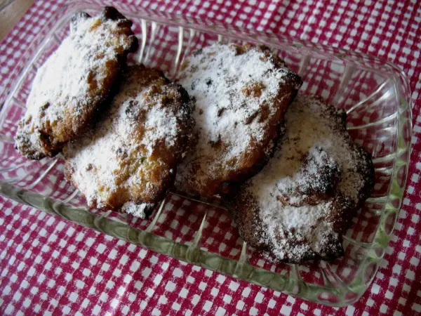 Zucchini-Apfel-Hafer-Cookies liegen auf einem Glasplatte, mit Puderzucker bestäubt, vor einem karierten Hintergrund.