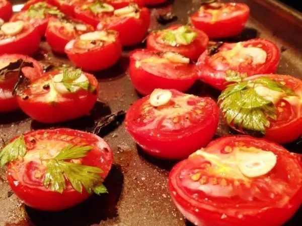 Rote Ofentomaten, mit Knoblauch und Kräutern belegt, werden auf einem Blech geröstet, um eine köstliche Beilage zu ergeben.