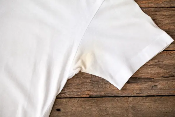 Ein weißes T-Shirt mit Deoflecken liegt auf einem Holztisch, bereit zur Reinigung oder Fleckentfernung.