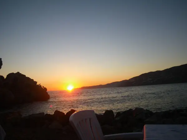 Sonnenuntergang über dem Meer, während der Hund am Ufer spielt. Entspanntes Ambiente an der Küste Spaniens mit Blick auf die Felsen.