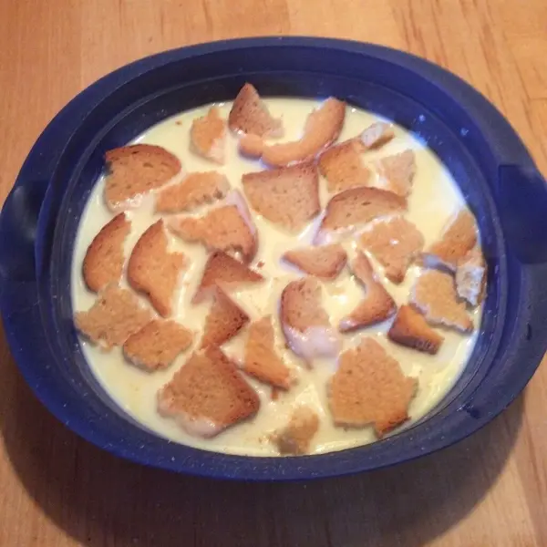 Eine blau-weiße Schale enthält eine cremige Buttermilchkaltschale, belegt mit knusprigen Brotwürfeln, auf einem Holzuntergrund.