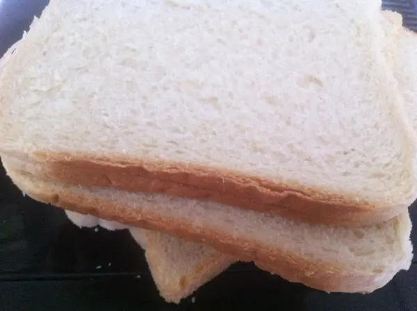 Zwei Scheiben frisches Toastbrot liegen übereinander auf einem Teller und zeigen eine goldene, leicht knusprige Oberfläche.