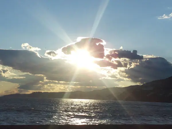 Ein strahlender Sonnenuntergang reflektiert auf dem Wasser, während Wolken den Himmel umgeben und eine ruhige Atmosphäre schaffen.