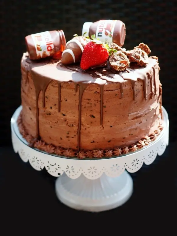 Ein schokoladiger Kuchen steht elegant auf einem Teller, dekoriert mit Nutellagläsern und frischen Erdbeeren.