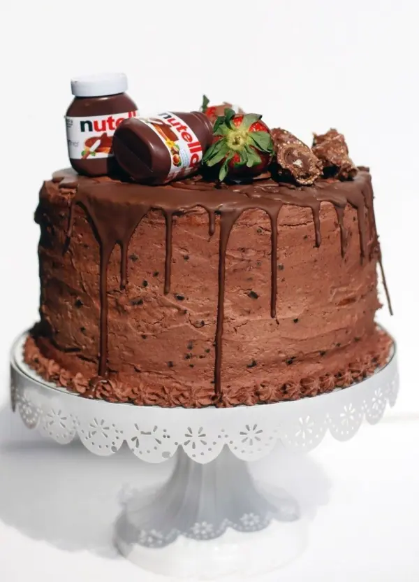 Ein Schokokuchen steht auf einem eleganten Teller, dekoriert mit Nutellagläsern und frischen Erdbeeren.