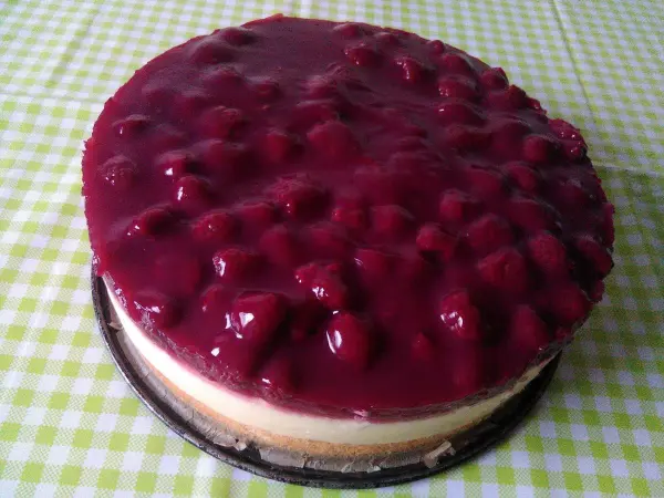 Eine Himbeer-Schmand-Torte liegt auf einem karierten Tisch, glänzend mit einer fruchtigen Schicht und frischen Himbeeren.