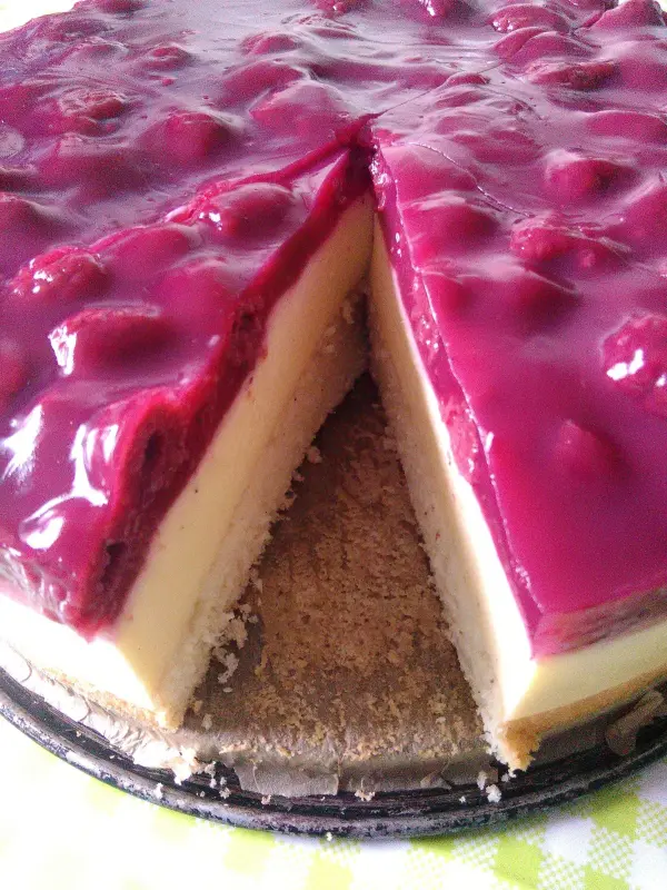 Die Himbeer-Schmand-Torte ist in Stücke geschnitten, mit einer glänzenden Himbeerglasur bedeckt und steht auf einem Teller.