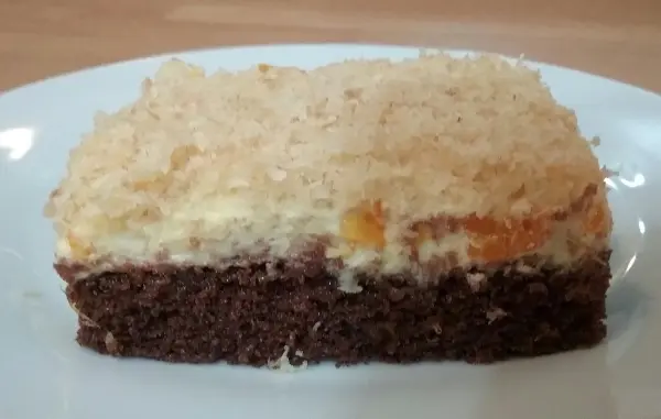 Ein Stück Sägespänekuchen mit Mandarinen sitzt auf einem weißen Teller, umgeben von einer hellen Küchentheke.