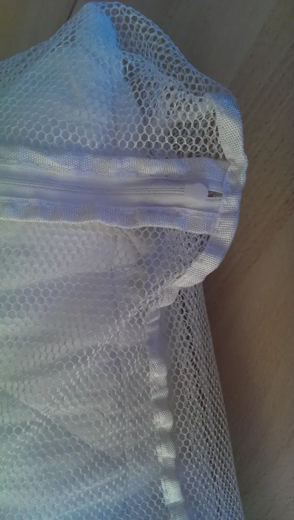 Ein Wäschenetz liegt mit dem Verschluss nach oben auf einem Tisch, bereit zum Einsatz, um Kleidung beim Waschen zu schützen.