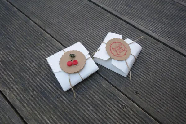 Weiße Keksschachteln aus Papier liegen auf einem Holztisch, mit dekorativen Anhängern und Schnur zusammengebunden.