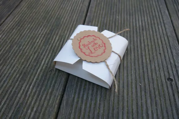 Eine dekorative Keksschachtel aus Papier liegt auf einer Holzoberfläche, elegant mit einer Schnur und einem Anhänger verziert.