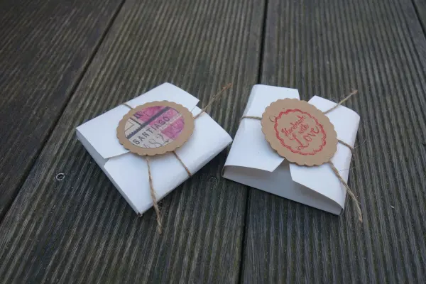 Zwei kleine, dekorative Keksschachteln aus Papier liegen auf einer Holzoberfläche, dekoriert mit Etiketten und Schnur.