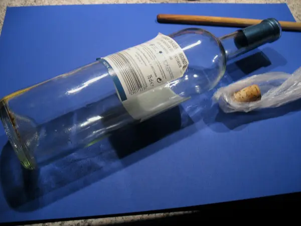 Eine Flasche liegt schräg auf einem blauen Untergrund, daneben liegt ein Korken, während ein Korkenzieher in der Nähe bereitliegt.