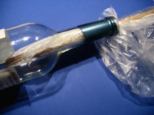 Eine Flasche mit einem Korken wird mit einem Plastikbeutel umwickelt, um den Korken sicher zu entfernen.