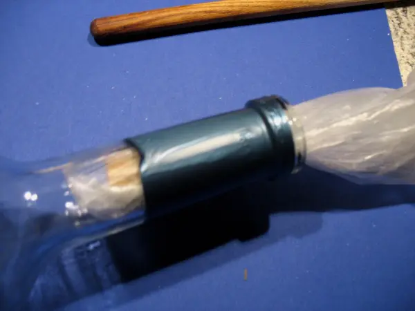 Ein Flaschenöffner entfernt einen Korken aus einer Flasche auf einem blauen Untergrund, umgeben von einem Holzstab.