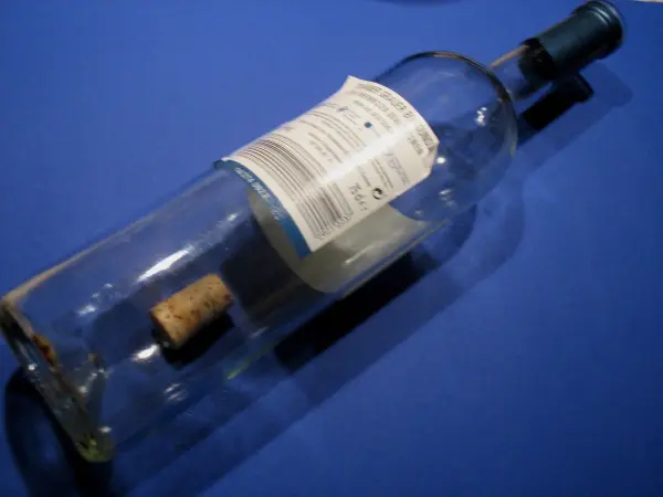 Eine Flasche liegt auf einem blauen Untergrund, der Korken befindet sich noch teilweise im Flaschenhals und wird entfernt.