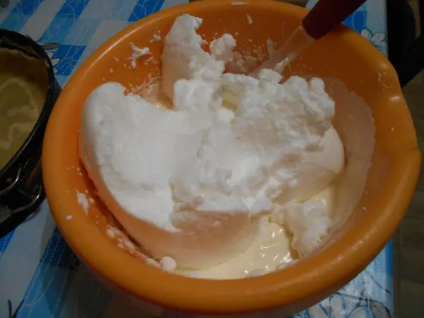Eine orange Schüssel mit einer Mischung aus geschlagenem Eiweiß und weiteren Zutaten für den Käsekuchen steht auf einem Tisch.