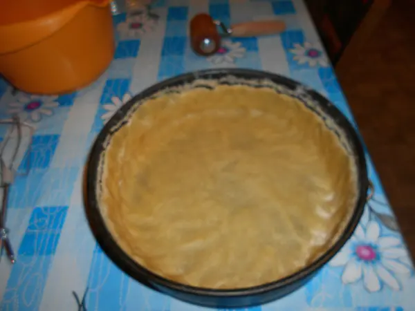 Ein unb Backblech mit einem vorbereiteten Boden für einen einfachen Käsekuchen steht auf einem blauen Tisch.