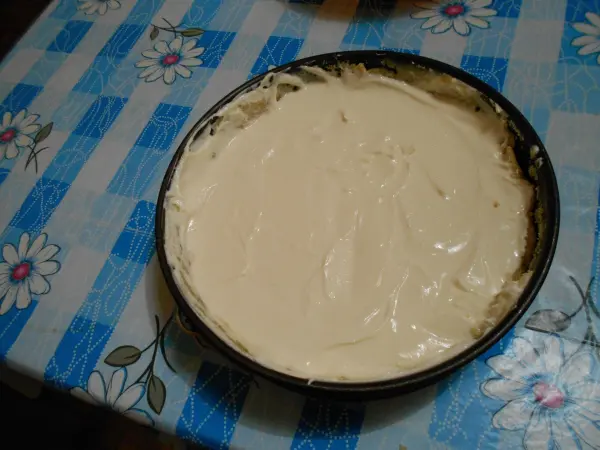 Ein Käsekuchen ohne Boden steht in einer runden Form auf einem bunten Tisch mit Blumenmuster.