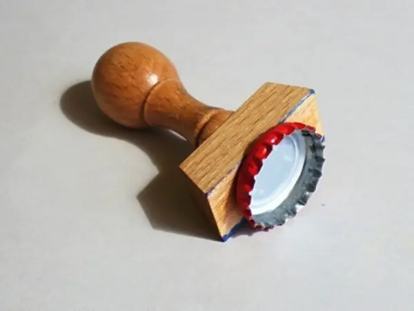 Ein Kettenanhänger aus Fimo wird mit einem Holzstempel geprägt, um kreative Designs zu erstellen. Der Stempel liegt auf einem neutralen Hintergrund.