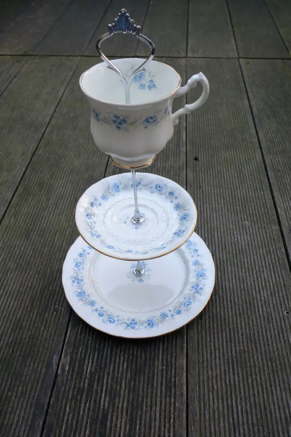 Eine Etagere aus altem Porzellan steht auf einem Holztisch, bestehend aus zwei Tellern und einer Tasse oben.