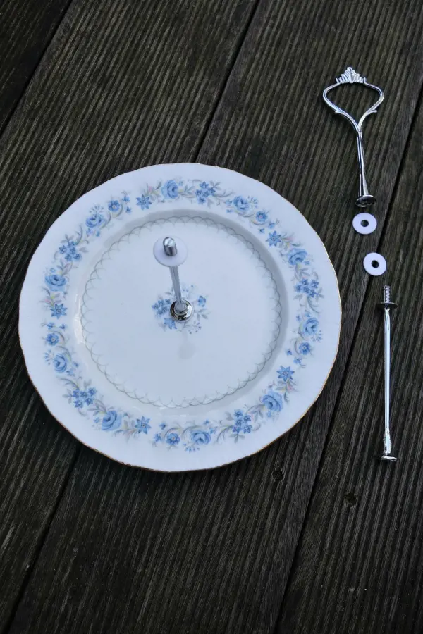 Ein Porzellanteller mit blauen Blumenmustern liegt auf einem Holzuntergrund, während Metallteile zum Bau einer Etagere daneben liegen.