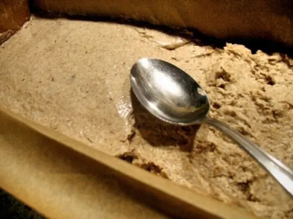 Ein silberner Löffel liegt in einer Form mit grobem, hellem Teig für knuspriges Roggen-Mischbrot. Der Teig wirkt frisch zubereitet.
