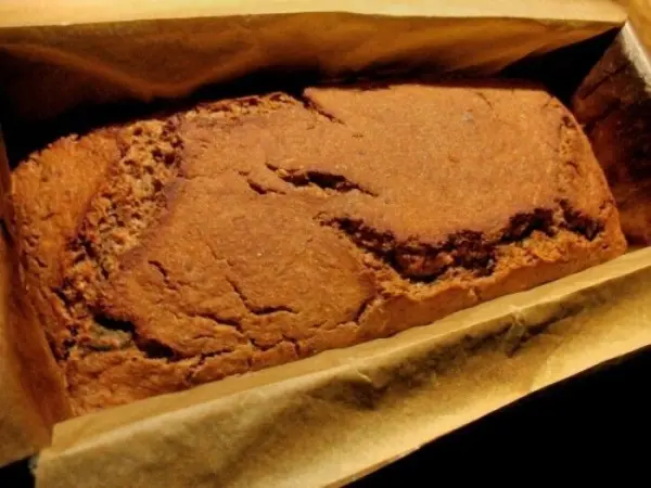 Ein frisch gebackenes Roggen-Mischbrot mit Kernen liegt in einer Papiertüte, umgeben von einer dunklen Umgebung.