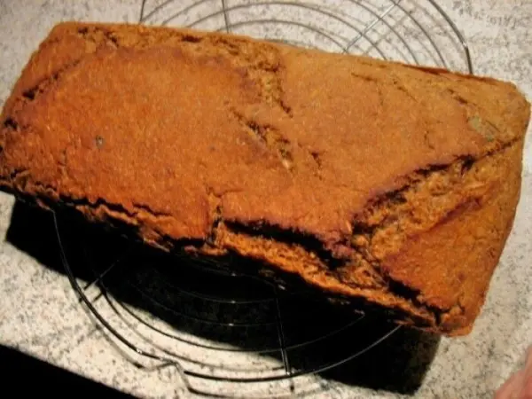 Ein knuspriges Roggen-Mischbrot mit Kernen liegt auf einem Gitter, um abzukühlen, in einer warmen Küchenszene.