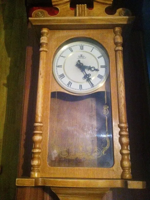Ein antiker Wanduhrenkasten aus Holz steht an der Wand, die Uhr zeigt die Zeit, umgeben von warmem Licht.