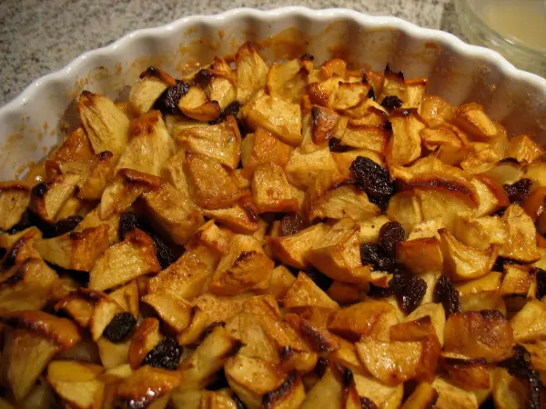Eine goldbraune Apfeltarte mit glänzenden Apfelstücken und Rosinen, frisch gebacken und im Tortenform präsentiert.