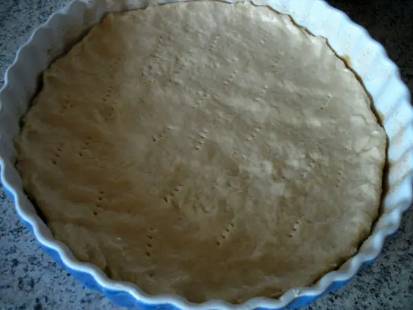 Eine Apfeltarte mit einem glatten Quark-Öl-Teig liegt in einer runden Form auf einer Arbeitsfläche, bereit zum Backen.