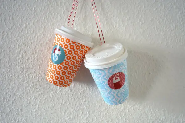 Bunte Coffee-to-go-Becher hängen dekorativ an einer Wand, gestaltet als Adventskalender mit nummerierten Etiketten.
