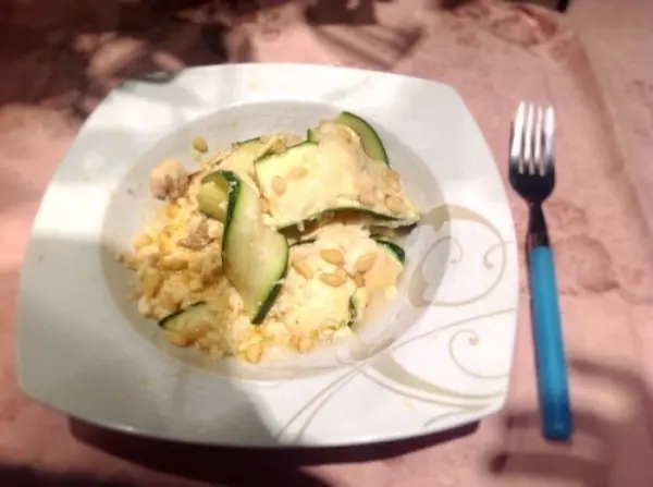 Der Zucchini-Hackfleisch-Auflauf liegt in einer weißen Schüssel, umgeben von zarten Zucchinistreifen und Hackfleisch auf einem Tisch.