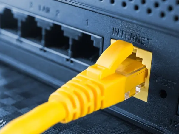 Ein gelbes Ethernet-Kabel ist mit einem Router verbunden, der das Internet bereitstellt, in einer modernen Wohnumgebung.