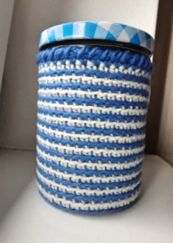 Ein blau-gestreifter Topflappen-Stulpen umhüllt ein Schraubglas und steht auf einer weißen Oberfläche.
