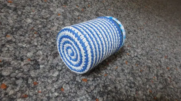 Ein blauer und weißer Topflappen-Stulpen liegt auf einer grauen, strukturierten Fläche, bereit zur Verwendung mit einem Schraubglas.