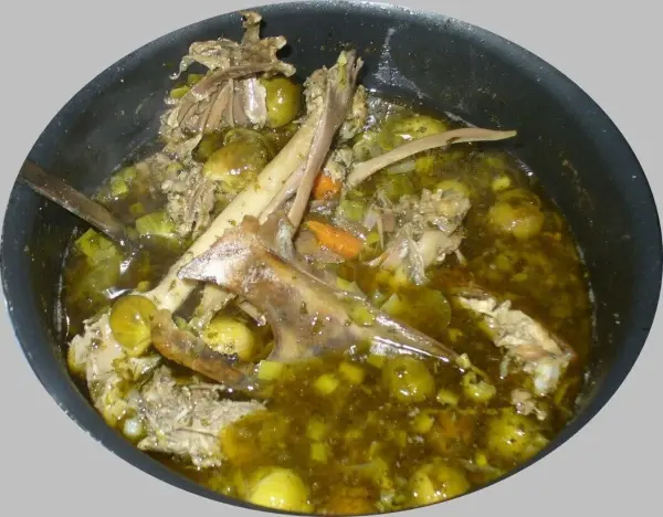Eine dicke Kraftsuppe aus Gänseknochen kocht in einem schwarzen Topf, umgeben von Gemüse und Brühe.
