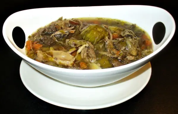 Eine weiße Schüssel voll mit Gänseknochen-Kraftsuppe, die köstlich dampft und mit Gemüse und Kräutern garniert ist.