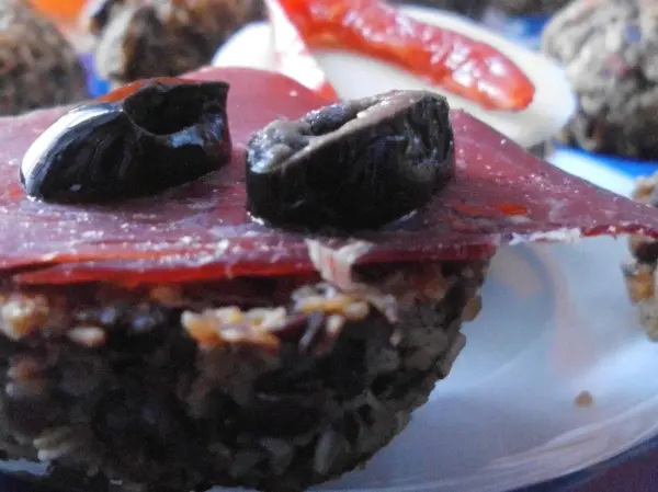 Haferflocken-Brötchen mit einer Schicht Wurst und Oliven auf einem weißen Teller, umgeben von buntem Gemüse.