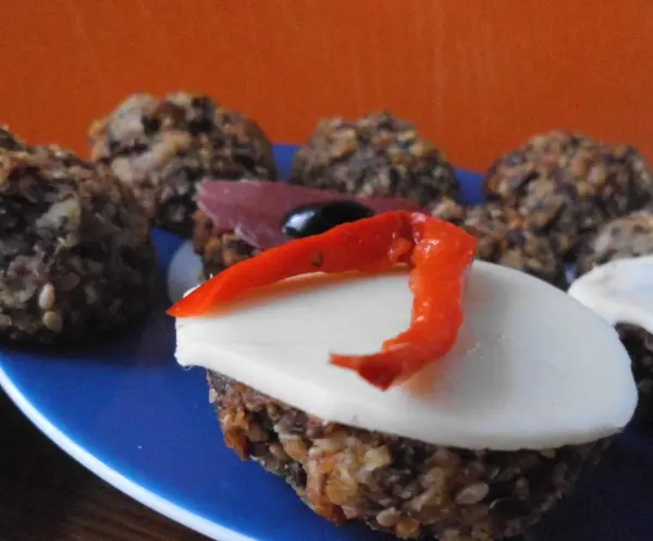 Ein Teller zeigt knusprige Haferflocken-Leinsamen-Brötchen, garniert mit Käse und Paprika, auf einem blaue Unterlage.