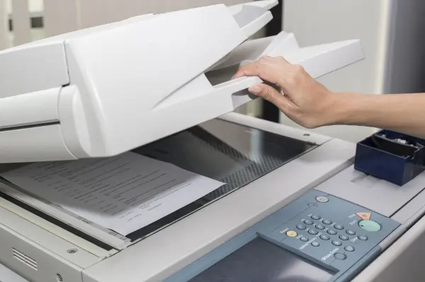 Ein Hand greift Papier aus einem Kopierer, um einseitig bedruckte Blätter für weiteres Drucken zu nutzen.