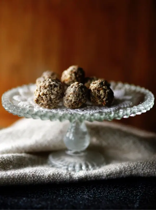 Kleine Müsli-Bällchen aus Hafer und Nüssen liegen appetitlich auf einem eleganten Glasstand, umgeben von einer neutralen Textilie.